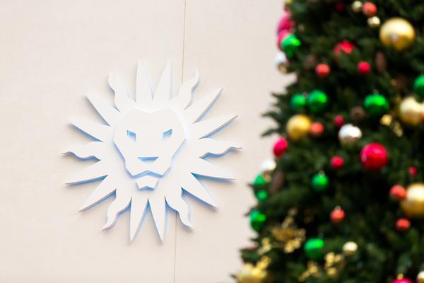 A cream wall with a sculpture of the LMU spirit mark on it, with a partial view of a blurry Christmas tree in the foregroung.